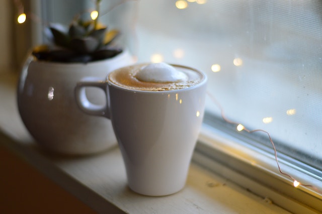 A cup of coffee beside a pot of succulent by the window.